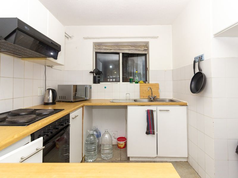 Compact kitchen featuring built-in oven, electric hob, extractor fan, and stainless steel sink with tiled splashbacks and laminate countertops.