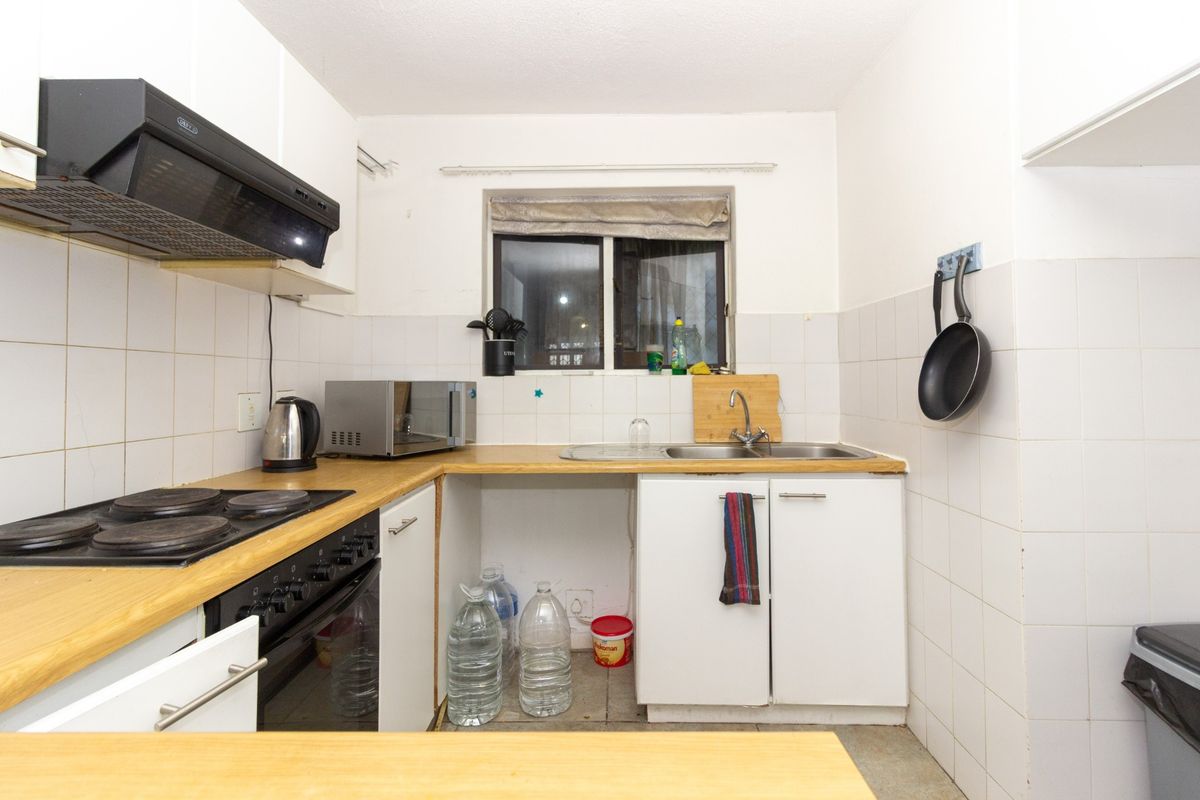 Compact kitchen featuring built-in oven, electric hob, extractor fan, and stainless steel sink with tiled splashbacks and laminate countertops.