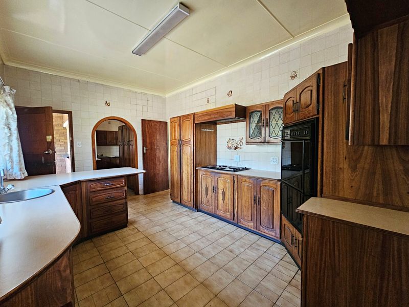 A spacious kitchen featuring traditional wooden cabinetry, built-in oven and hob, tiled backsplash, and a functional layout with an adjacent scullery area.