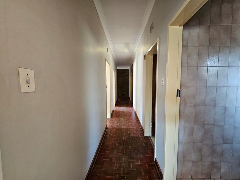 A long, empty hallway featuring traditional parquet flooring, coved cornicing, and neutral wall finishes, providing access to multiple rooms.