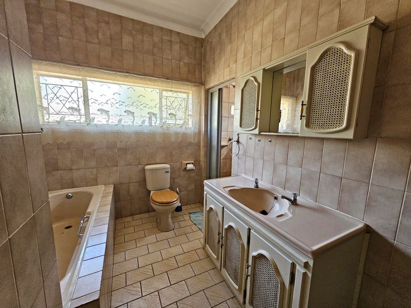 A dated bathroom featuring a built-in vanity with integrated basin, tiled bathtub, and toilet, finished with neutral ceramic wall and floor tiles.