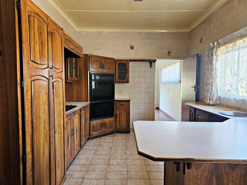 A dated kitchen featuring traditional wooden cabinetry, built-in oven, tiled splashbacks, and tiled flooring, offering potential for a modern renovation.