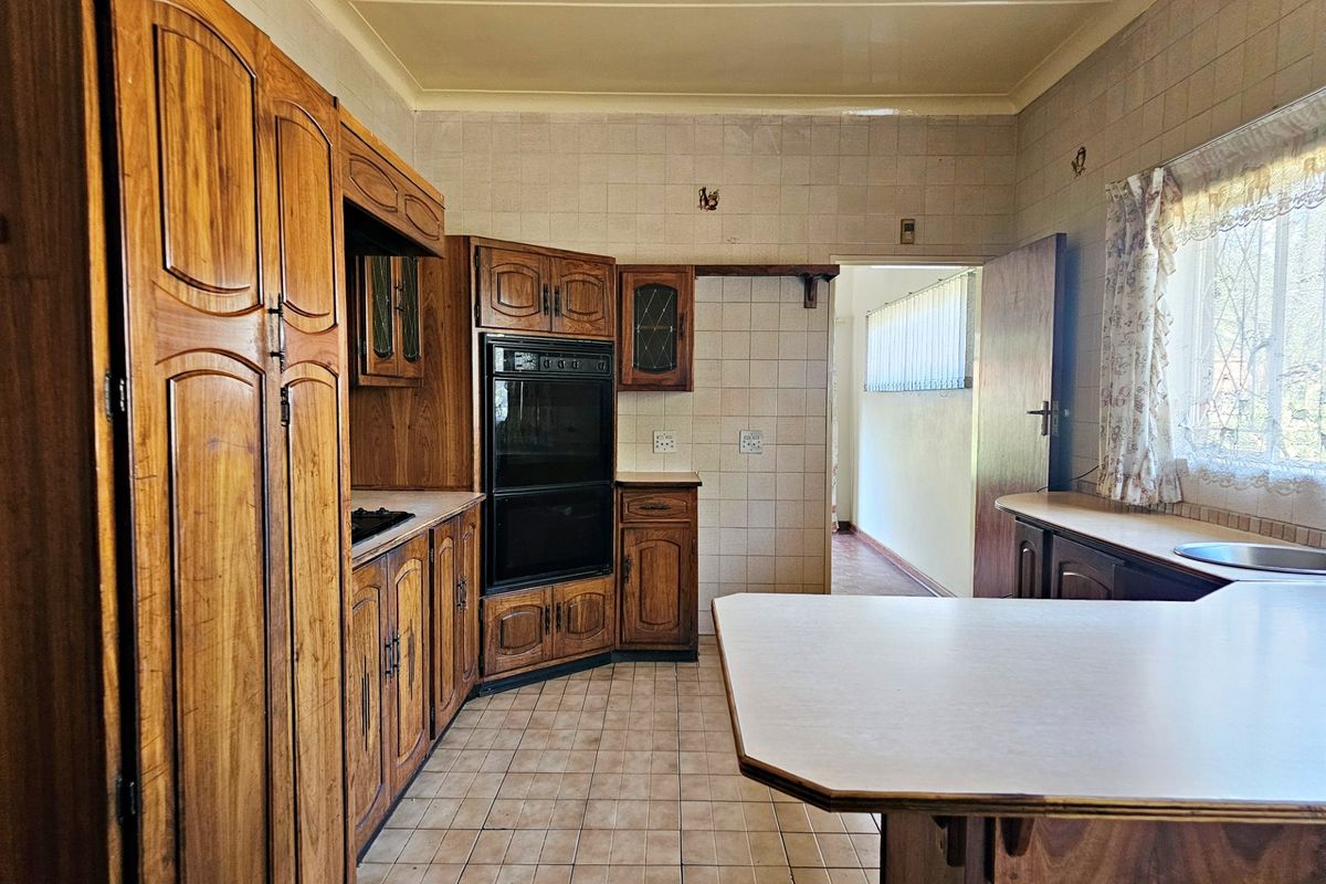A dated kitchen featuring traditional wooden cabinetry, built-in oven, tiled splashbacks, and tiled flooring, offering potential for a modern renovation.