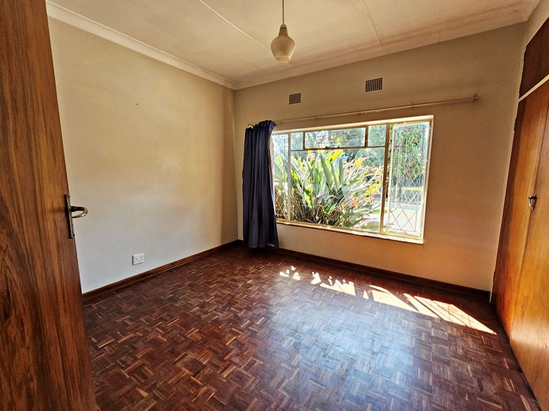 A vacant bedroom featuring classic parquet flooring, built-in wooden cupboards, and a large window providing natural light.