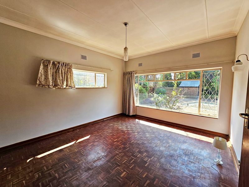 A spacious, empty living room featuring original parquet flooring, large steel-framed windows, and classic coved cornicing, offering a blank canvas for renovation.