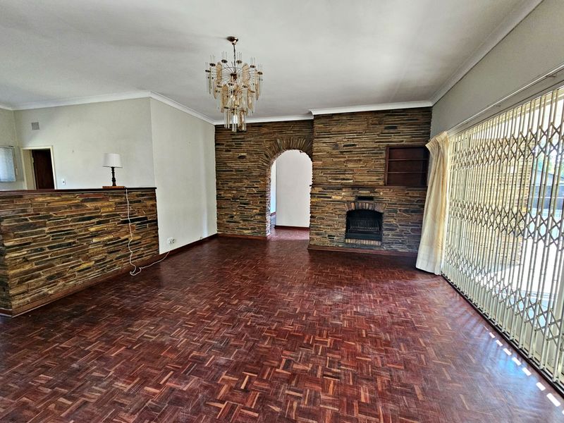 Spacious living room featuring classic parquet flooring, a prominent stone fireplace, and a stone feature wall with an arched entryway.