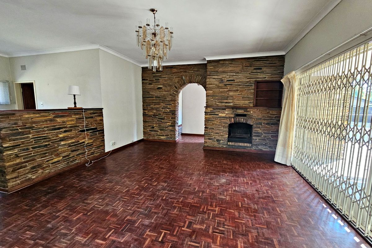 Spacious living room featuring classic parquet flooring, a prominent stone fireplace, and a stone feature wall with an arched entryway.