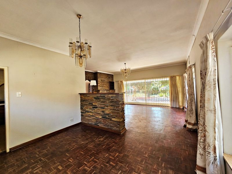 Spacious living area featuring parquet flooring, a stone-clad feature wall, and decorative chandeliers, offering a versatile layout with direct access to the exterior.