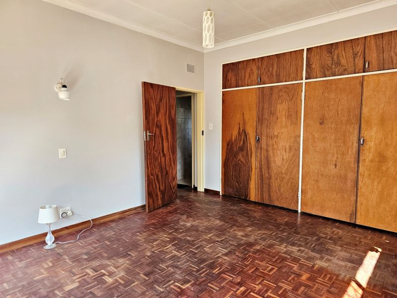 A spacious bedroom featuring original parquet flooring, built-in wooden cupboards, and a neutral color palette, offering a blank canvas for renovation.