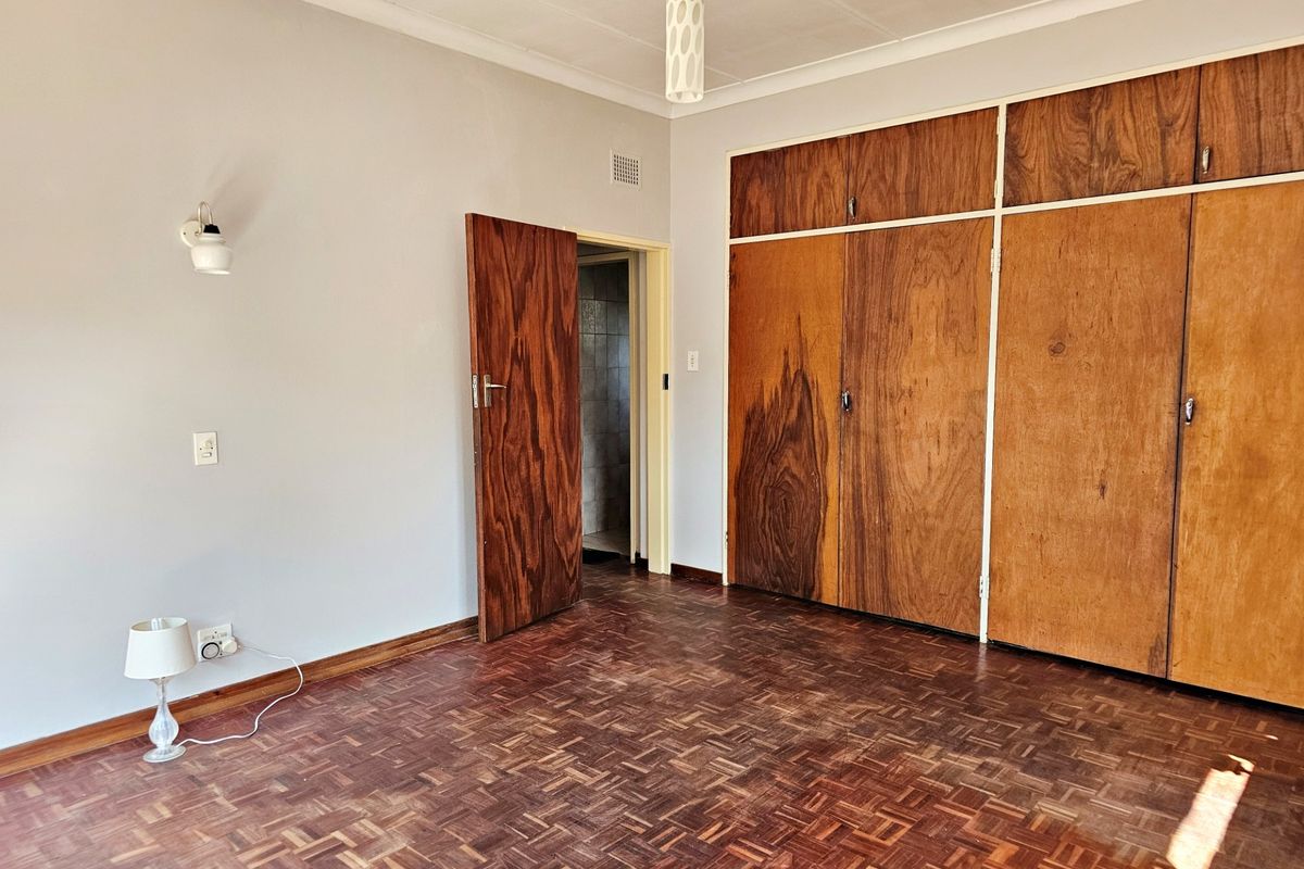 A spacious bedroom featuring original parquet flooring, built-in wooden cupboards, and a neutral color palette, offering a blank canvas for renovation.