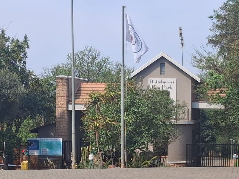 The entrance gate to Buffelspoort Eco Park, featuring stone masonry accents, a tiled roof structure, and a flagpole.