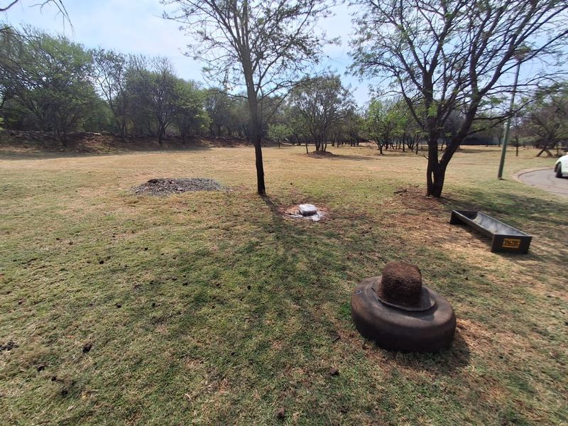 A view of a spacious, grass-covered residential plot featuring mature trees and open land, suitable for future development.
