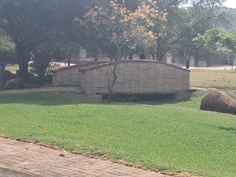 A landscaped garden area featuring a decorative stone-clad pedestrian bridge and paved walkway set within a residential property.