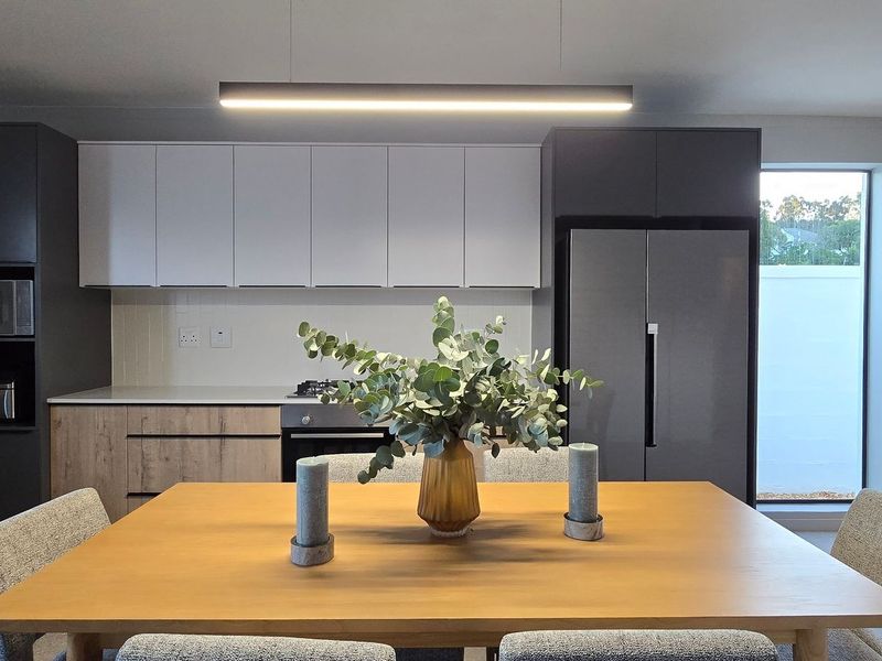 Modern open-plan kitchen featuring sleek two-tone cabinetry, integrated appliances, and contemporary pendant lighting, seamlessly flowing into the dining area.