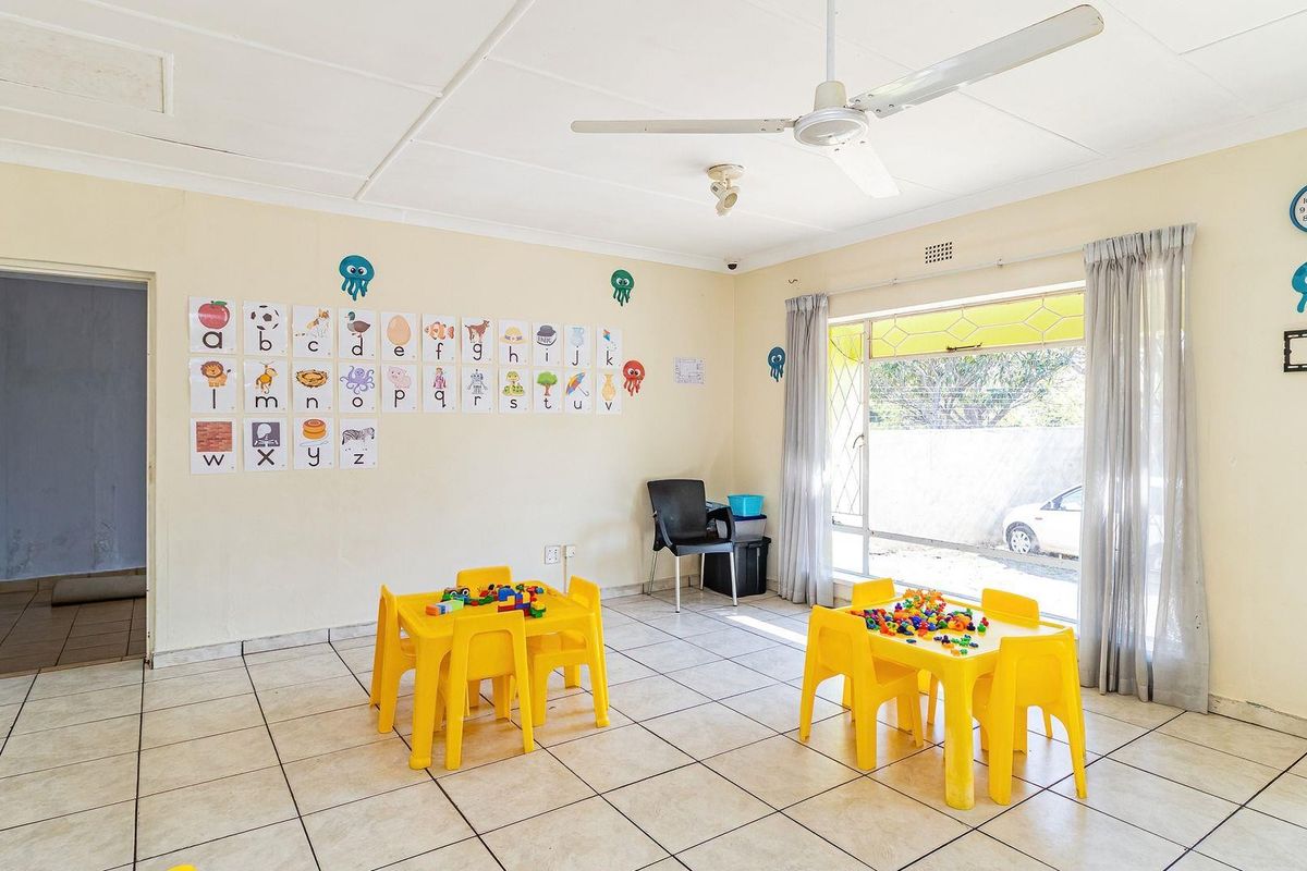 A multi-purpose room featuring tiled flooring, a ceiling fan, and large windows, currently utilized as a play area.