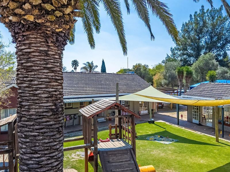 A spacious rear garden area featuring a well-maintained lawn, paved pathways, and a large shade sail providing cover for outdoor activities.