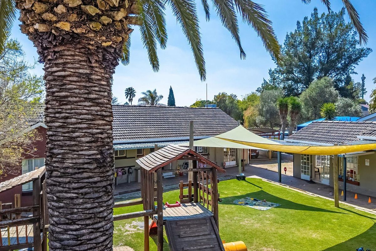 A spacious rear garden area featuring a well-maintained lawn, paved pathways, and a large shade sail providing cover for outdoor activities.