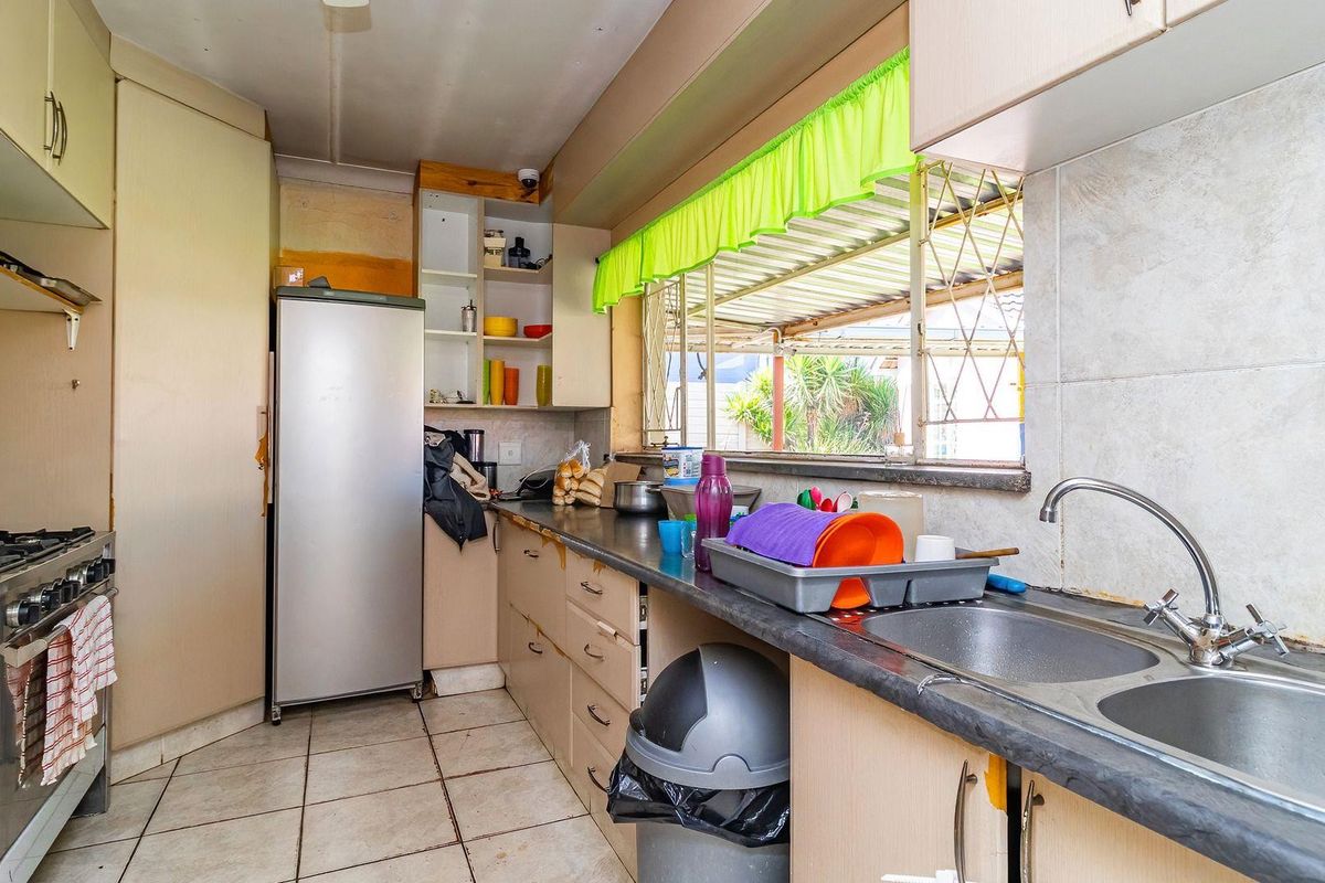 A functional kitchen featuring built-in cabinetry, a double bowl sink, and a gas stove, with tiled flooring and splashbacks throughout.