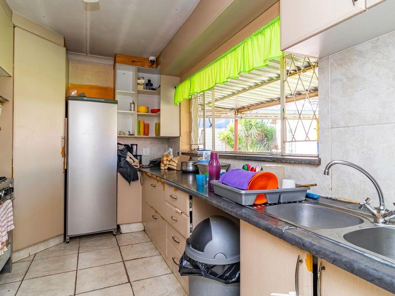 A functional kitchen featuring built-in cabinetry, a double bowl sink, and a gas stove, with tiled flooring and splashbacks throughout.