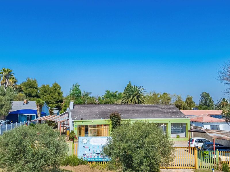 Aerial view of the property frontage featuring a single-story house with a tiled roof, perimeter fencing, and a paved driveway with carport.