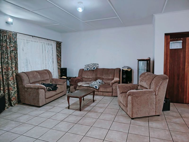 A spacious living room featuring neutral tiled flooring and a classic wooden door, offering a functional and well-lit area for relaxation.
