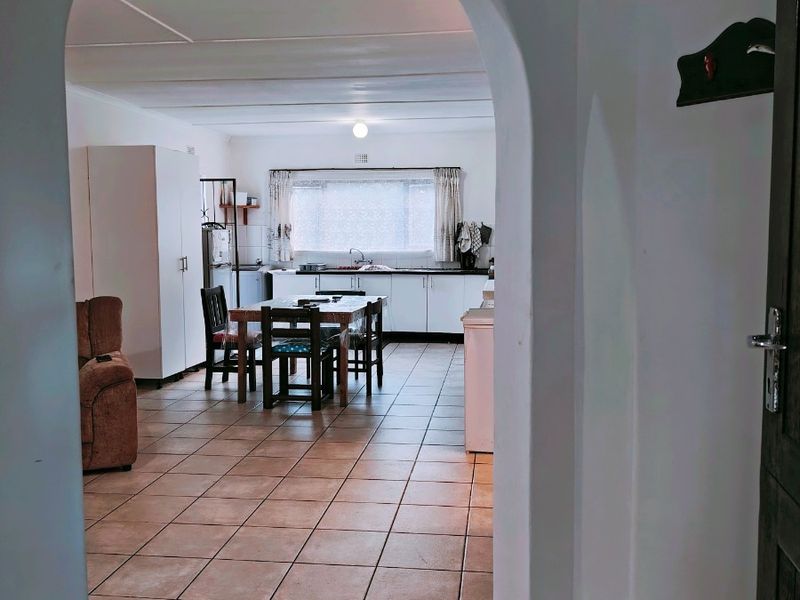 An open-plan kitchen and dining area viewed through an arched doorway, featuring tiled flooring and functional cabinetry.