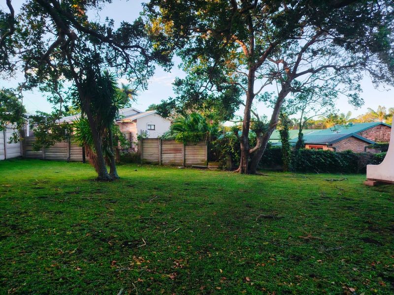 A spacious, private backyard garden featuring established mature trees, a well-maintained lawn, and secure perimeter boundary walling.