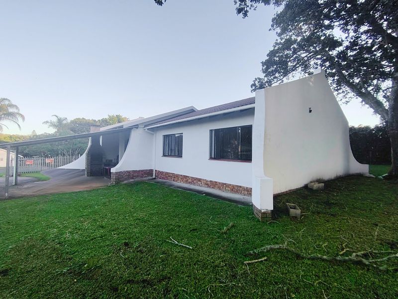 Rear view of the house featuring a covered patio area with a built-in braai, brick base detailing, and a spacious lawn.
