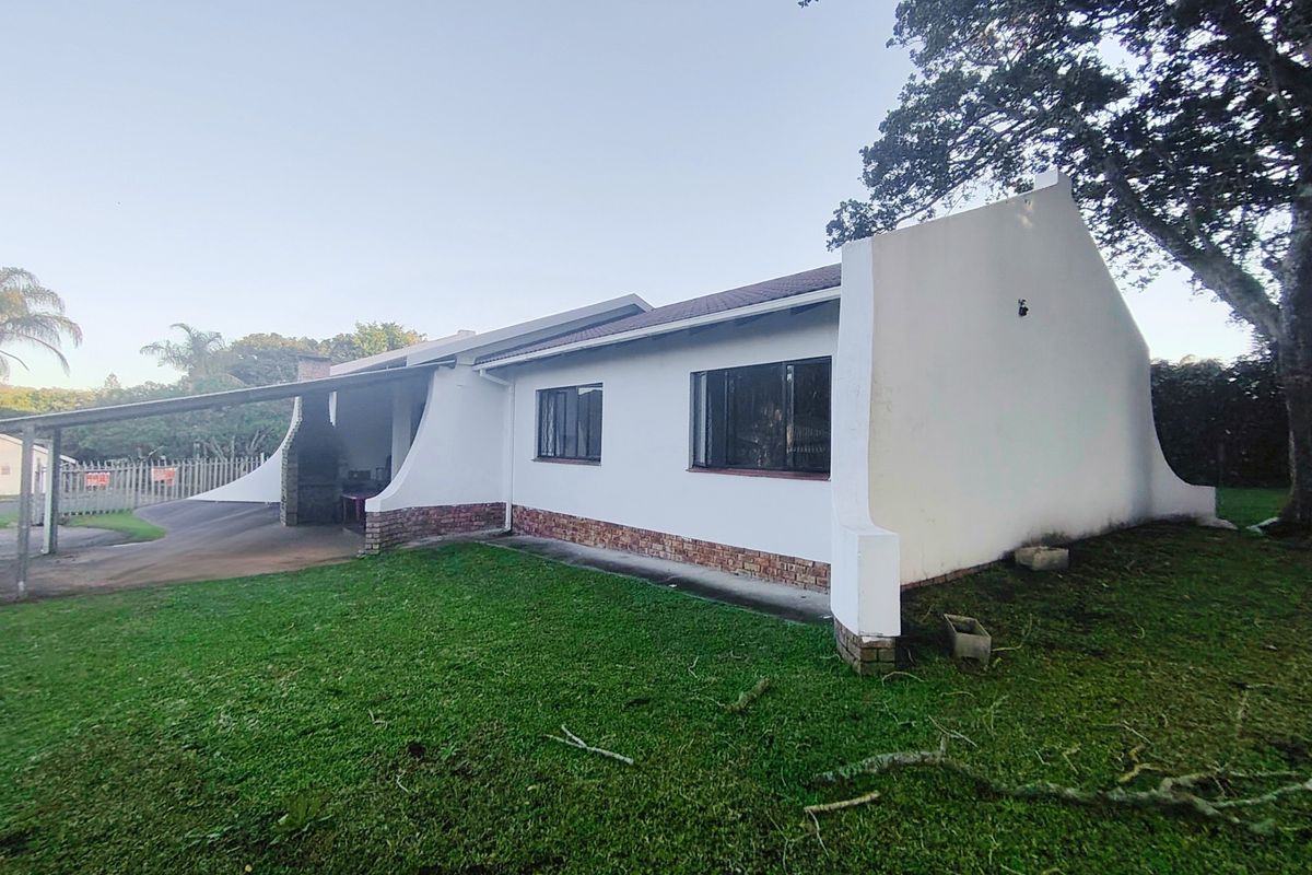 Rear view of the house featuring a covered patio area with a built-in braai, brick base detailing, and a spacious lawn.