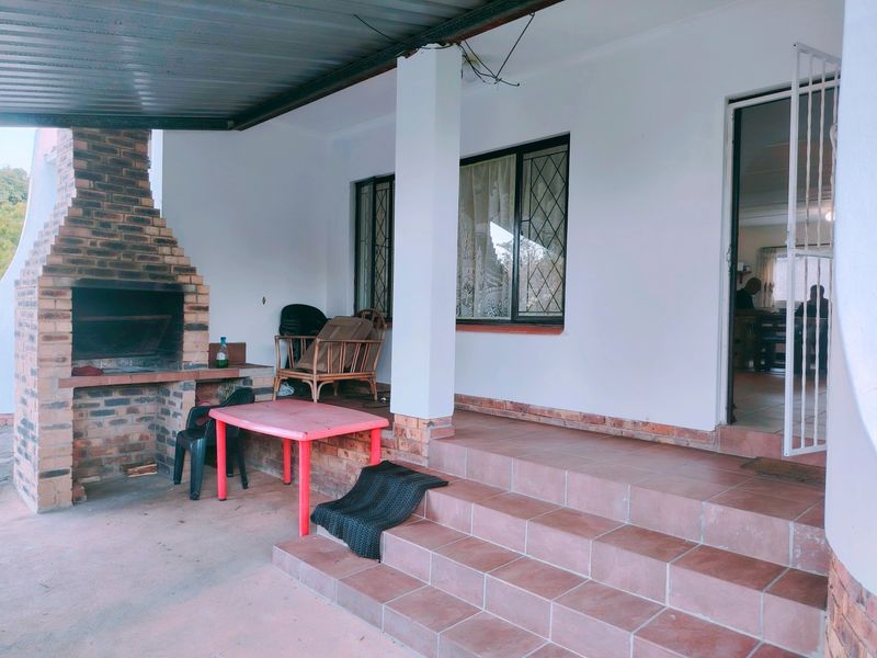 Covered outdoor patio featuring a built-in brick braai, tiled steps, and direct access to the interior through a security gate.