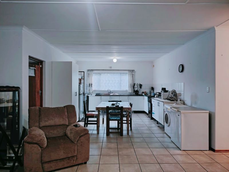 An open-plan living and kitchen area featuring tiled flooring, functional cabinetry, and a central dining space, offering a practical layout for daily living.