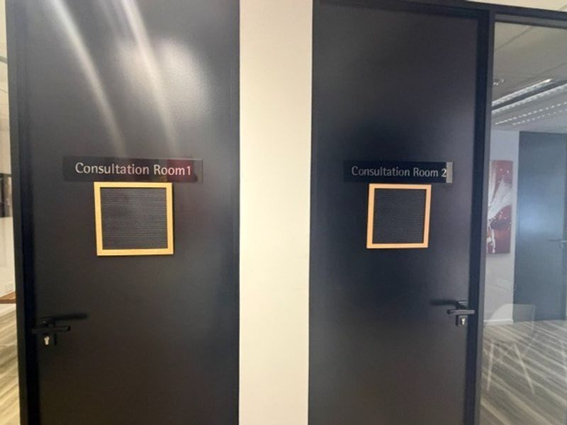 A hallway view featuring two modern black consultation room doors with professional signage and durable laminate flooring.