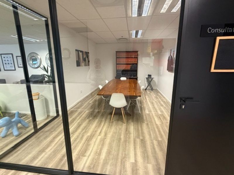 A professional office consultation room featuring modern glass partitioning, wood-look flooring, and recessed ceiling lighting, creating a bright and functional workspace.