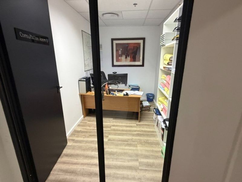 A functional office consultation room featuring laminate flooring, a suspended ceiling with recessed lighting, and integrated built-in shelving.