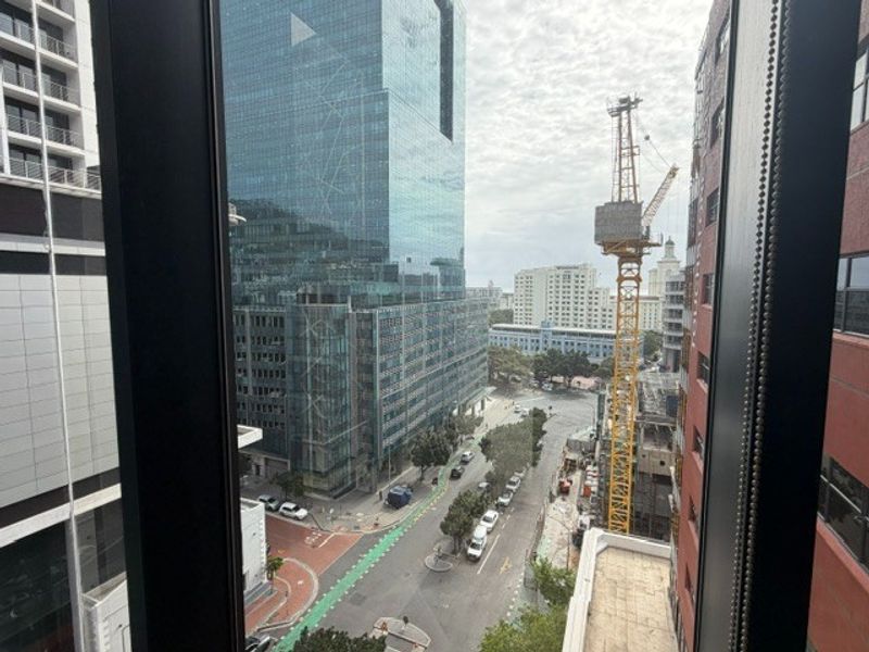 An elevated urban view from an office window overlooking a city street, surrounding high-rise buildings, and active construction site.