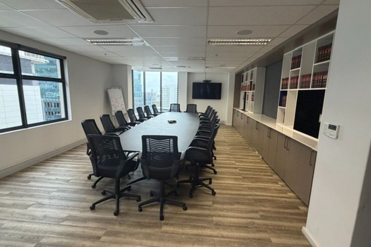 A professional boardroom featuring a large conference table, built-in storage cabinetry, suspended ceiling with integrated lighting, and large windows with city views.
