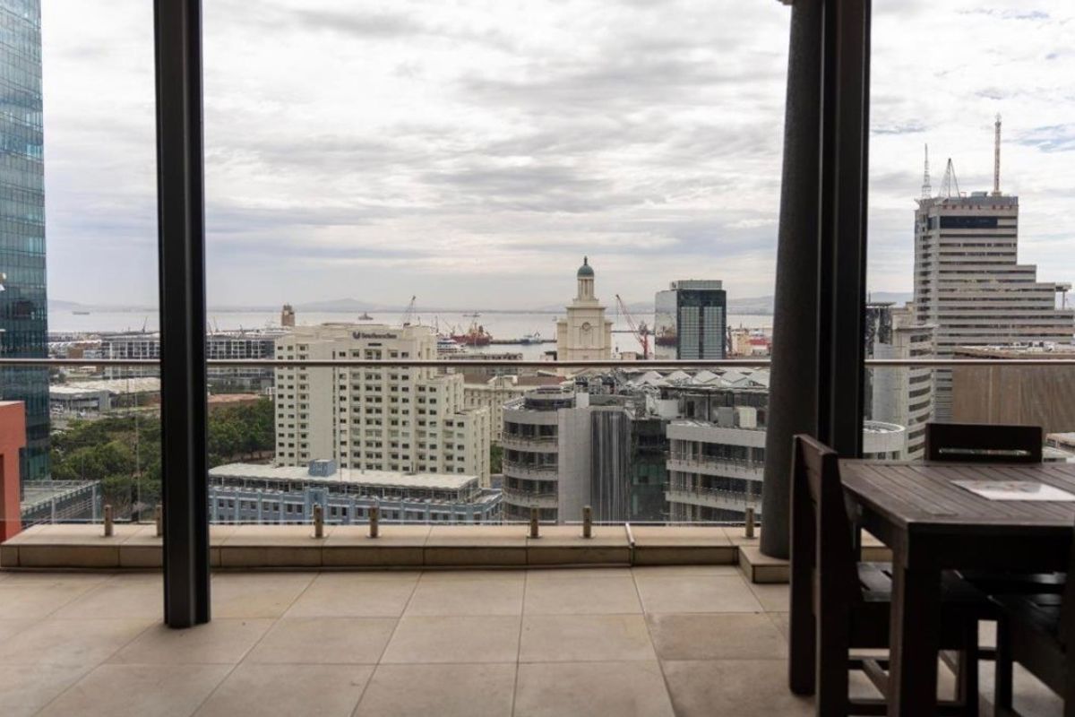 A spacious covered balcony featuring tiled flooring and a modern glass balustrade, offering expansive elevated city and harbour views.