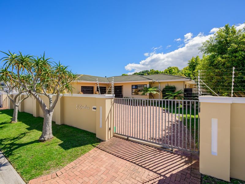 Front exterior view of the property featuring a paved driveway, secure metal gate, and perimeter wall with electric fencing.