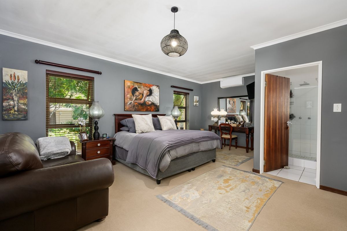 Spacious bedroom featuring neutral carpeting, grey walls, an en-suite bathroom, and an integrated air conditioning unit.