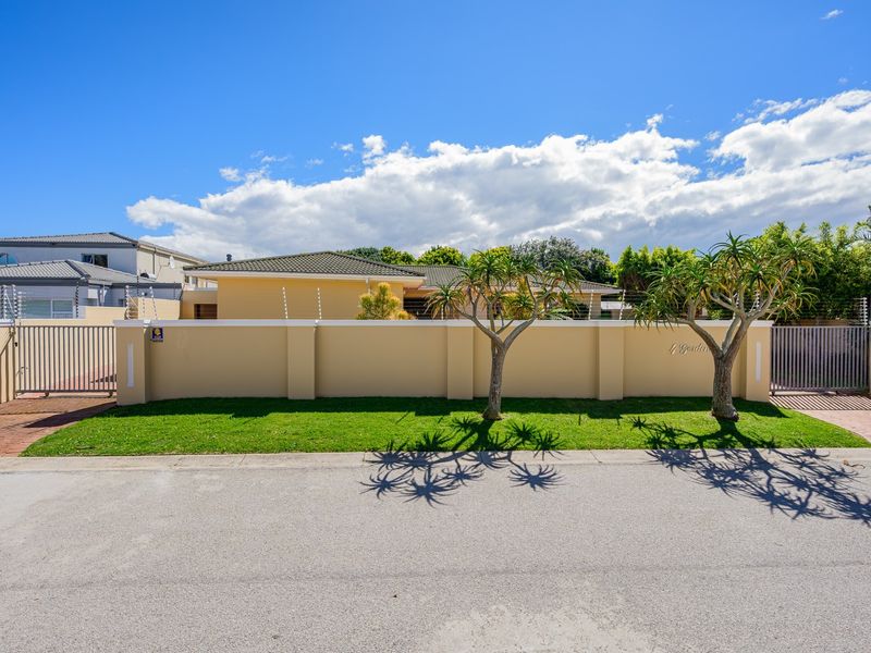 Front exterior view of the property featuring a secure perimeter wall with electric fencing, paved driveway access, and well-maintained landscaping.