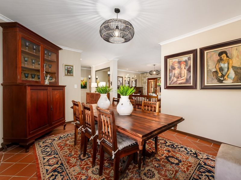 A well-maintained dining room featuring terracotta floor tiles, coved cornicing, and a central pendant light fixture, flowing into an adjacent living area.