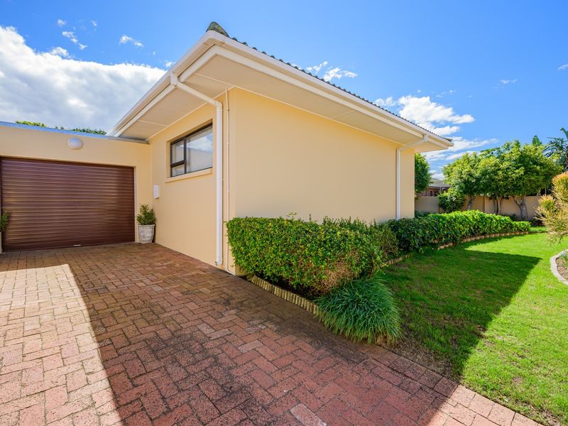 Front exterior view featuring a paved driveway, roller garage door, and well-maintained garden area with established landscaping.