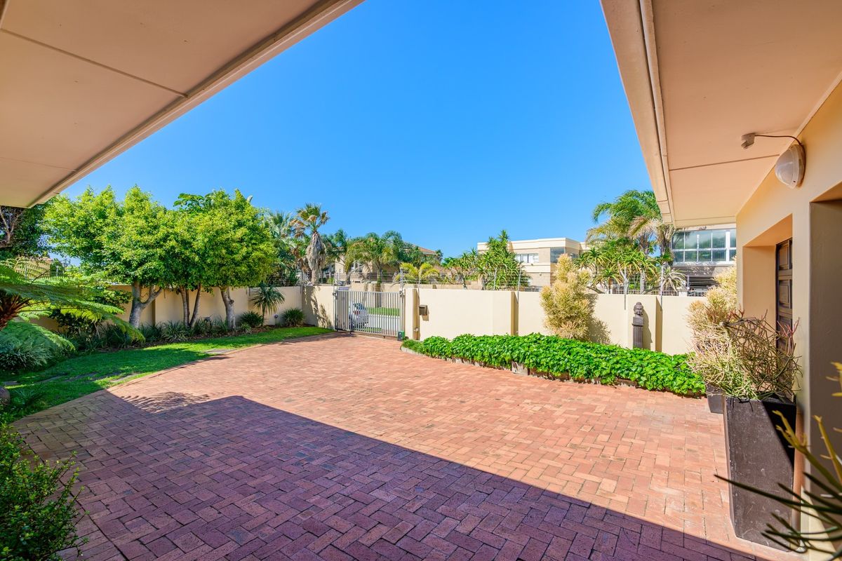 A well-maintained rear courtyard featuring brick paving, a secure perimeter wall with electric fencing, and a covered patio area.