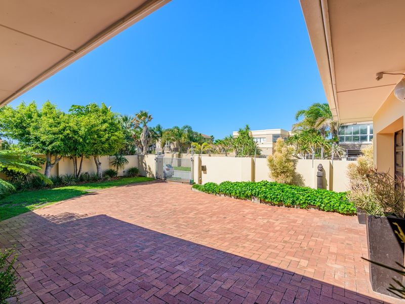 A well-maintained rear courtyard featuring brick paving, a secure perimeter wall with electric fencing, and a covered patio area.