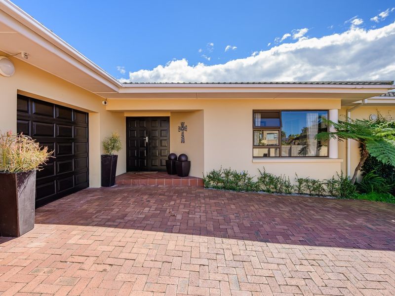 Front elevation of the property featuring a brick paved driveway, double garage, and a covered entrance with double doors.