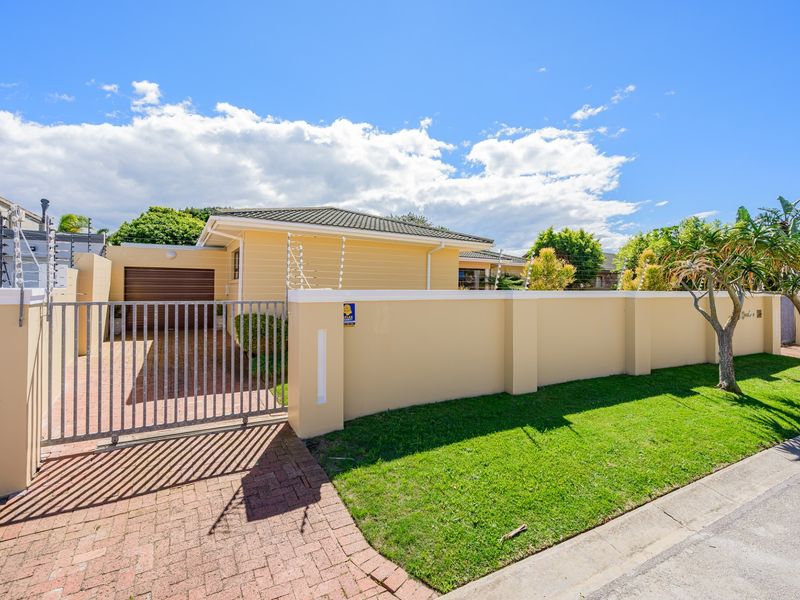 Front view of the property featuring a paved driveway, secure metal gate, perimeter wall with electric fencing, and a single garage.