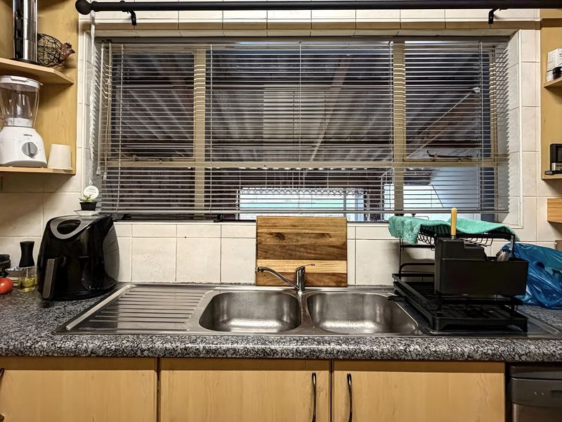 A functional kitchen sink area featuring a double bowl stainless steel sink, laminate countertops, and tiled splashback with built-in cabinetry.