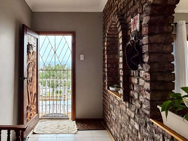 Entrance hall featuring a distinctive exposed brick wall with arched openings, tiled flooring, and a decorative carved wooden door leading to the exterior.