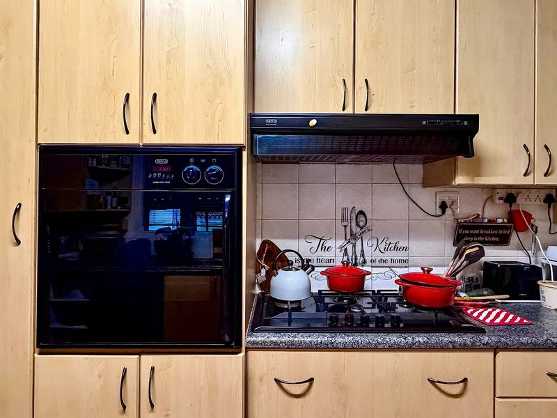 A functional kitchen area featuring light wood cabinetry, a built-in oven, gas hob, extractor fan, and granite countertops with a tiled backsplash.