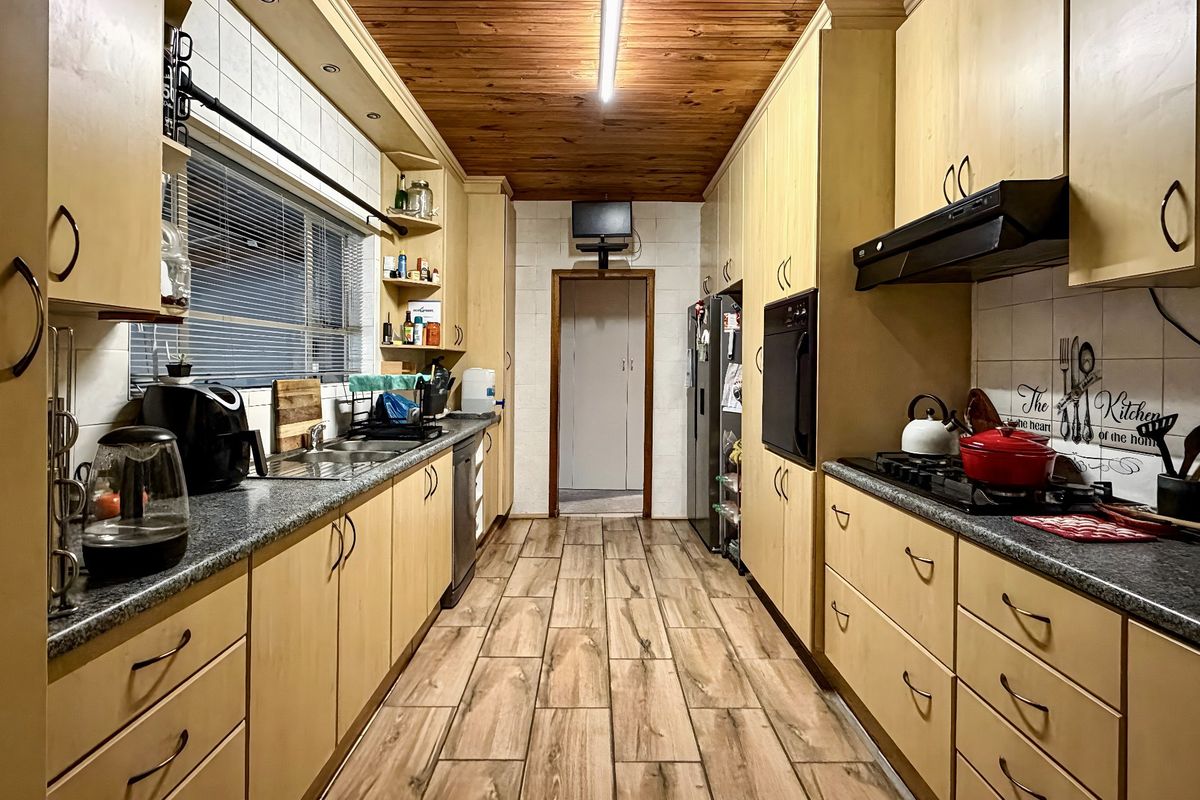 Galley-style kitchen featuring light wood cabinetry, granite-look laminate countertops, built-in oven, gas hob, and a distinctive timber-paneled ceiling.